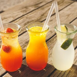 Close-up of three refreshing beverages with citrus, strawberries, and lime on a sunny wooden table.