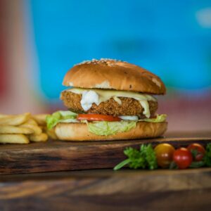 Close-up of a chicken burger with fresh vegetables and fries on a wooden table.