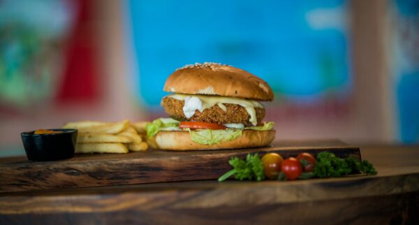 Close-up of a chicken burger with fresh vegetables and fries on a wooden table.